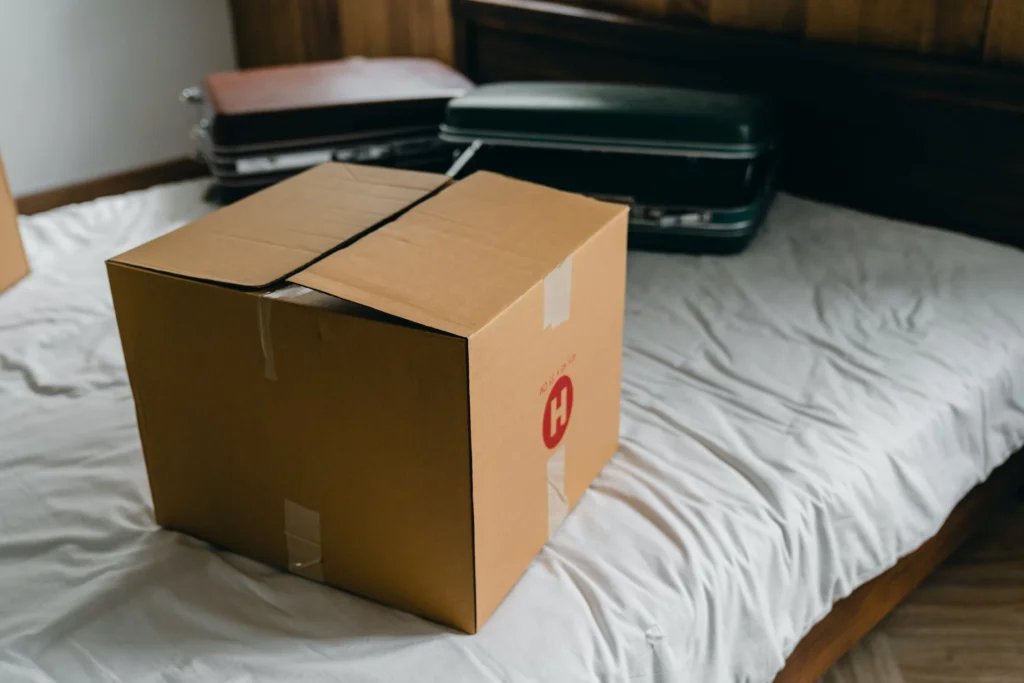 A moving box on top of a bed with some suitcases in the background