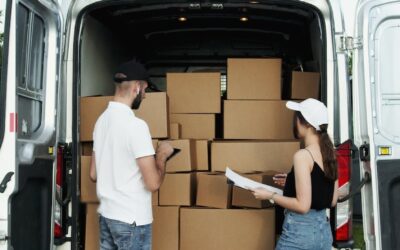 A moving van packed full of moving boxes with two people standing behind it.